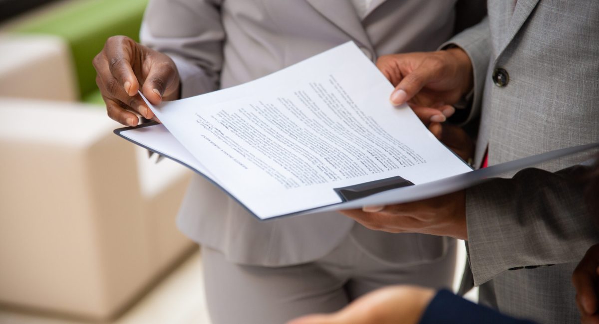 Diverse business partners reading contract together. Business man and woman wearing formal suits, standing and holding open folder with document. Agreement concept